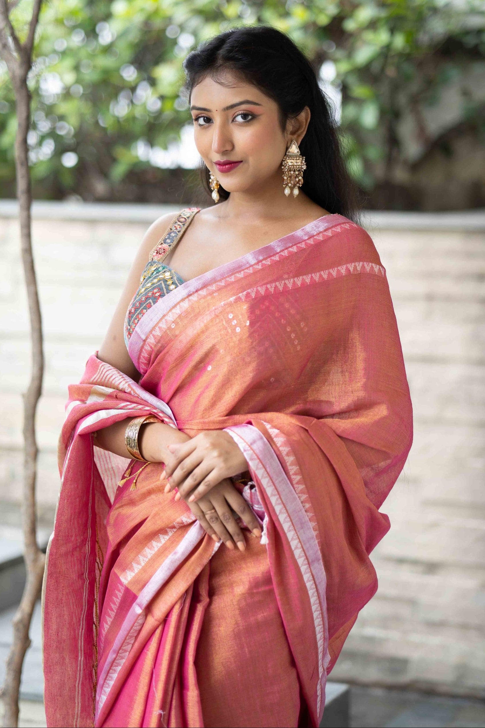 Woman in a pink saree standing outdoors with greenery in the background
