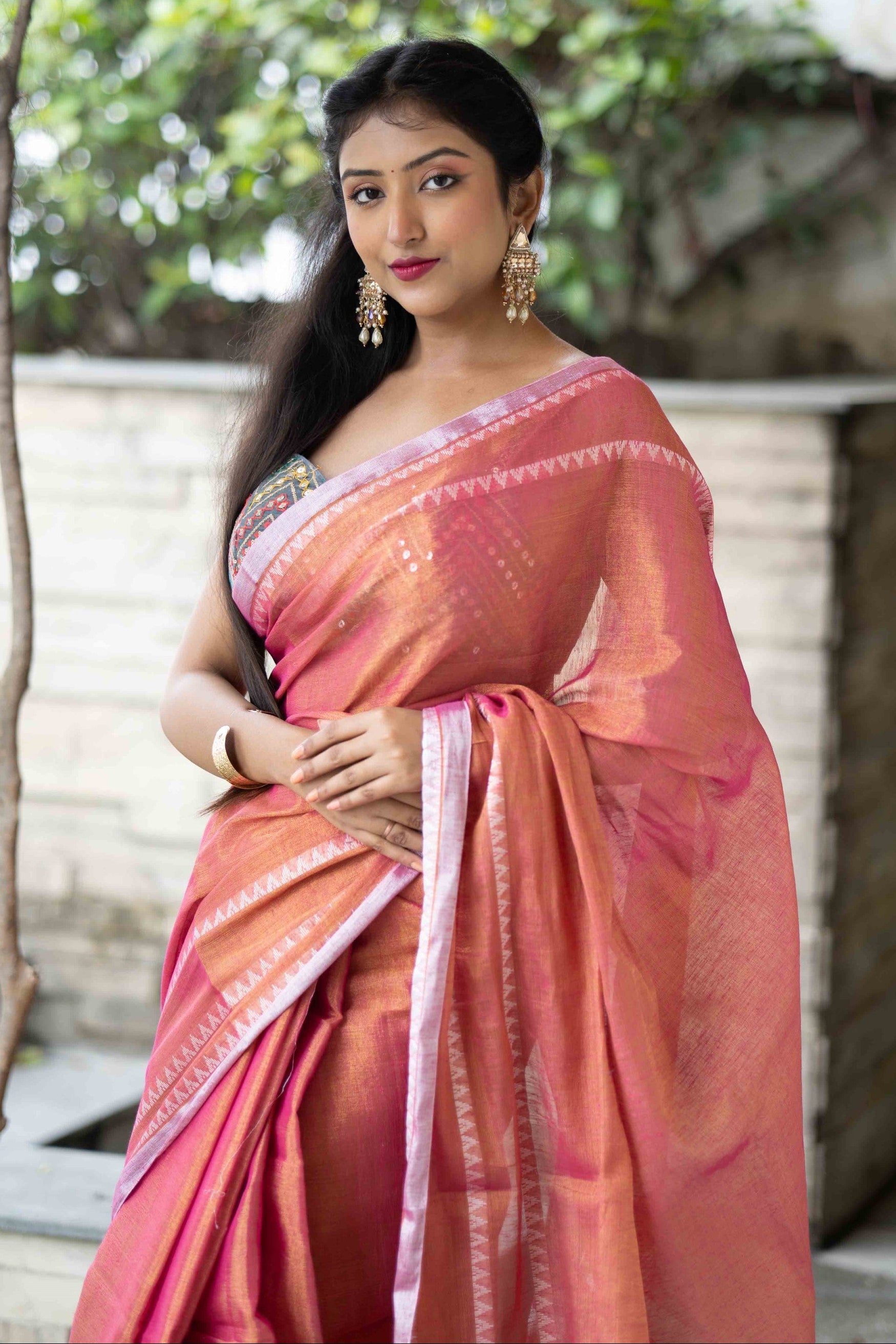 Woman in a pink saree standing outdoors with greenery in the background